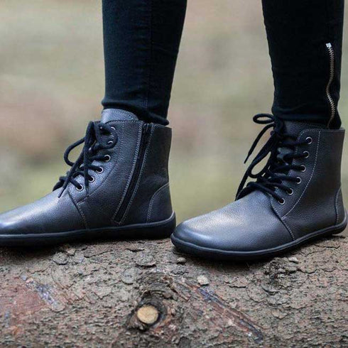 En person står på en trädstam i skogen med ett par barfotaskor för vintern från Be Lenka som heter Nord i svart färg.