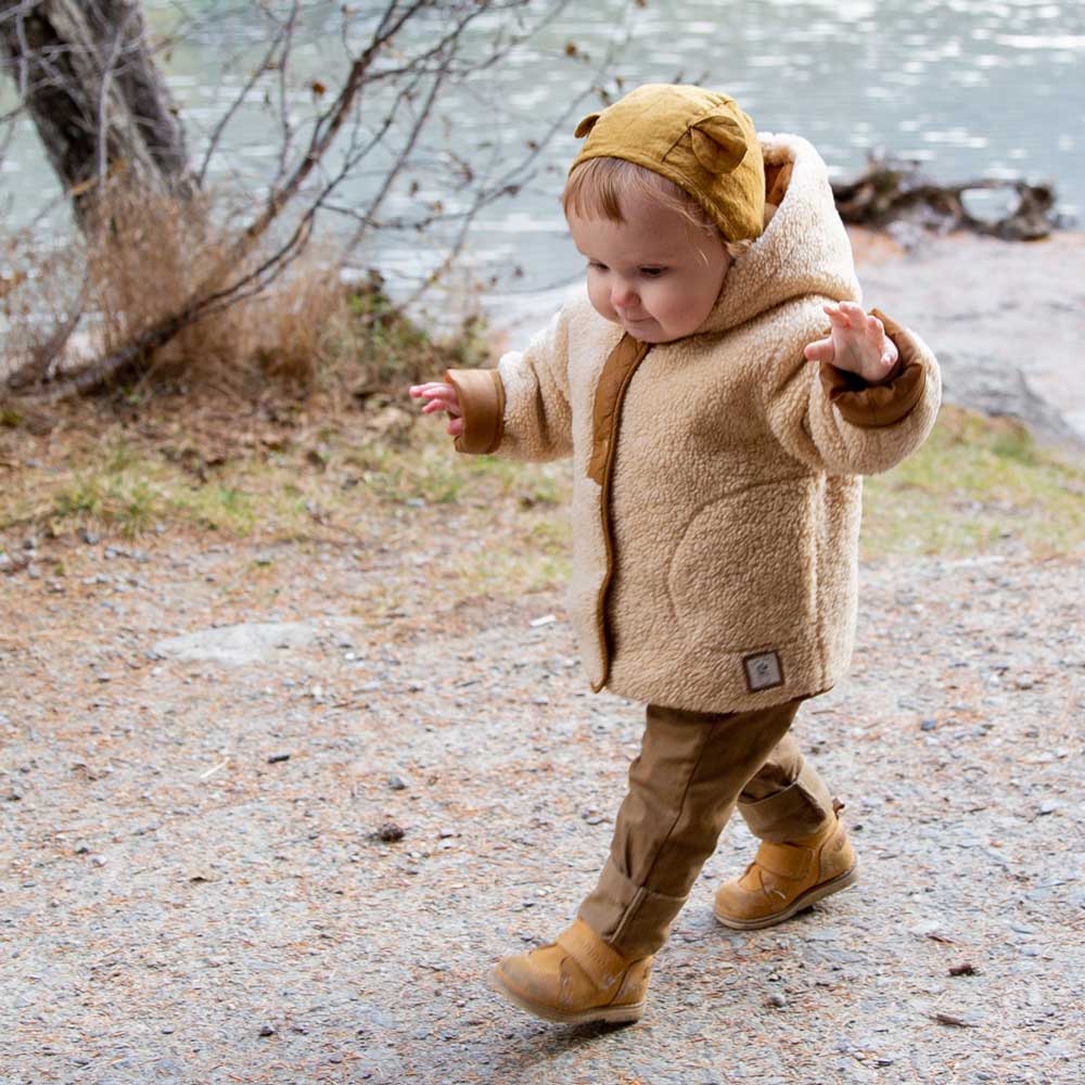 Ett litet barn går på en stig i naturen bredvid en sjö i ett par gula läragåskor.