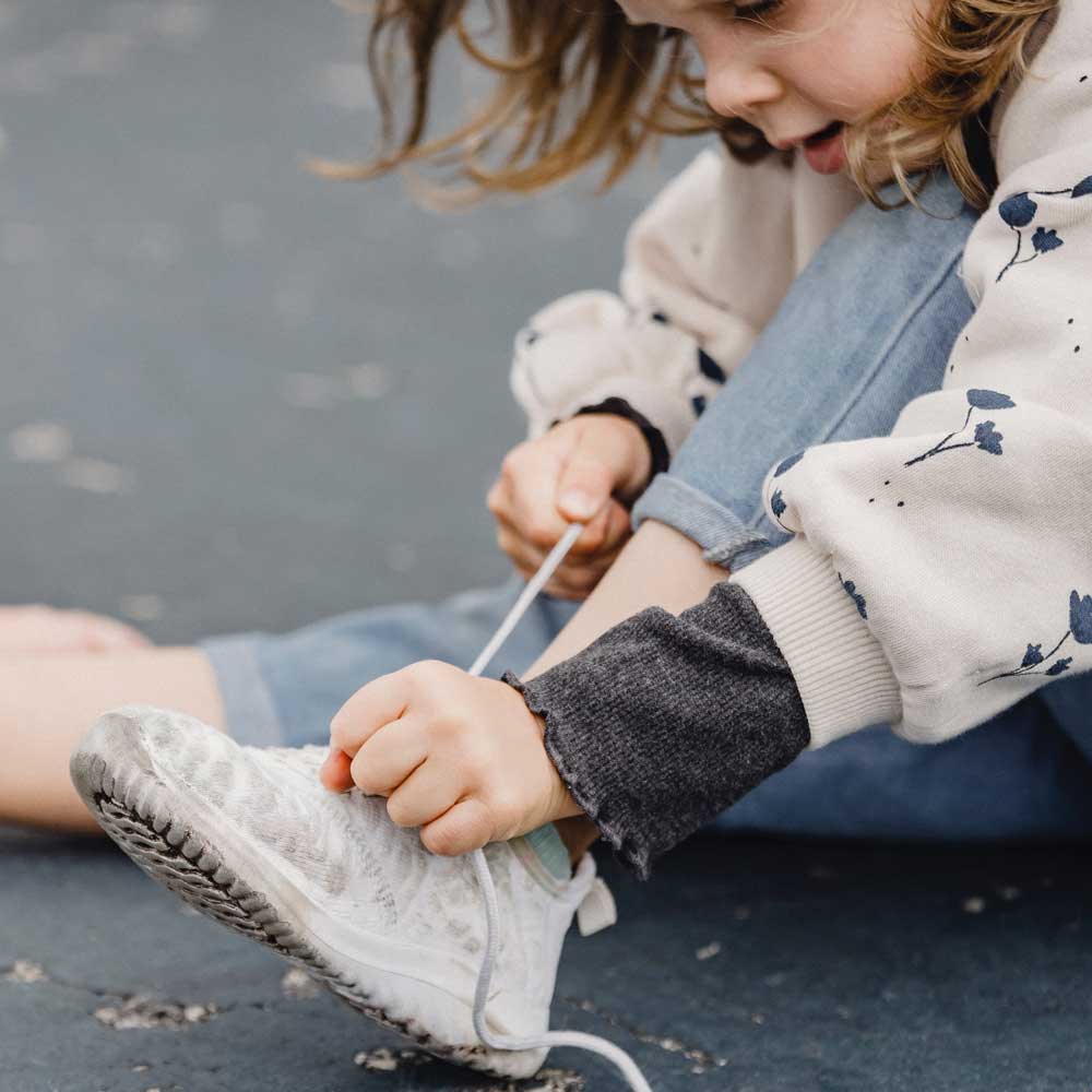 Ett barn knyter sina barnskor med ett skosnören men har problem att få det bra.