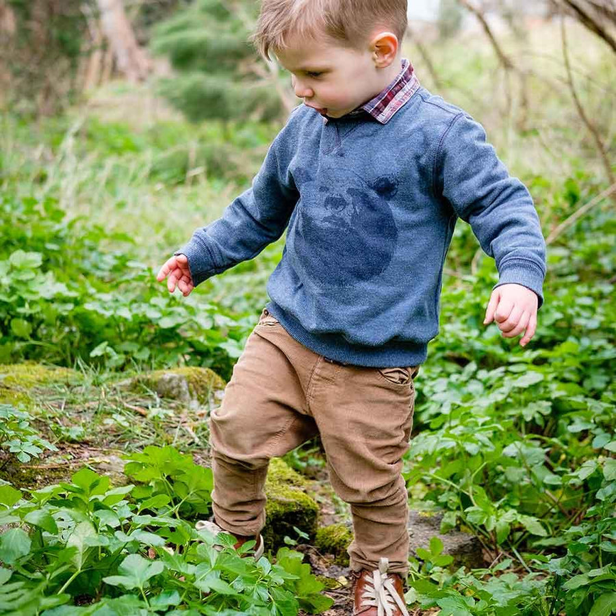 En pojke leker i skogen och utforskar naturen i fina barnkläder med slitstarka byxor och fina barnskor.