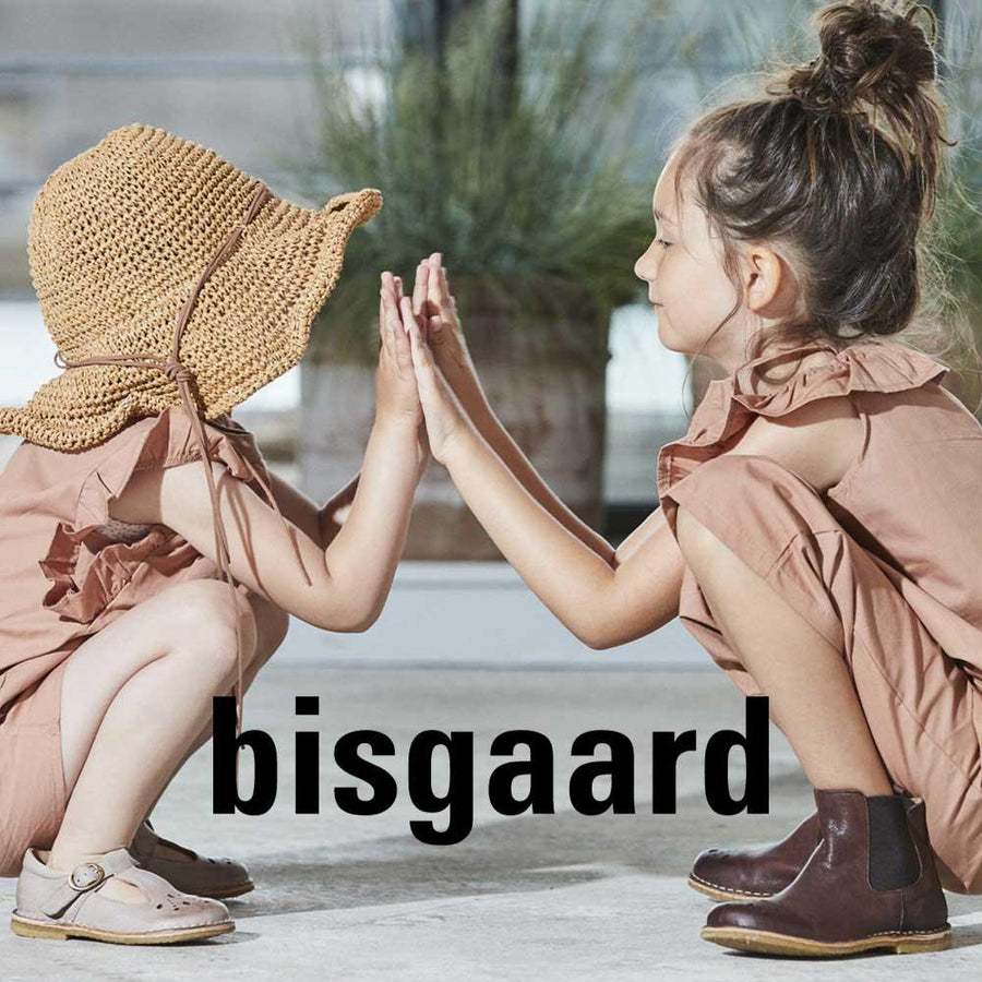 Två barn sitter på huk i barnskor från Bisgaard och gör hi-five med varandra.
