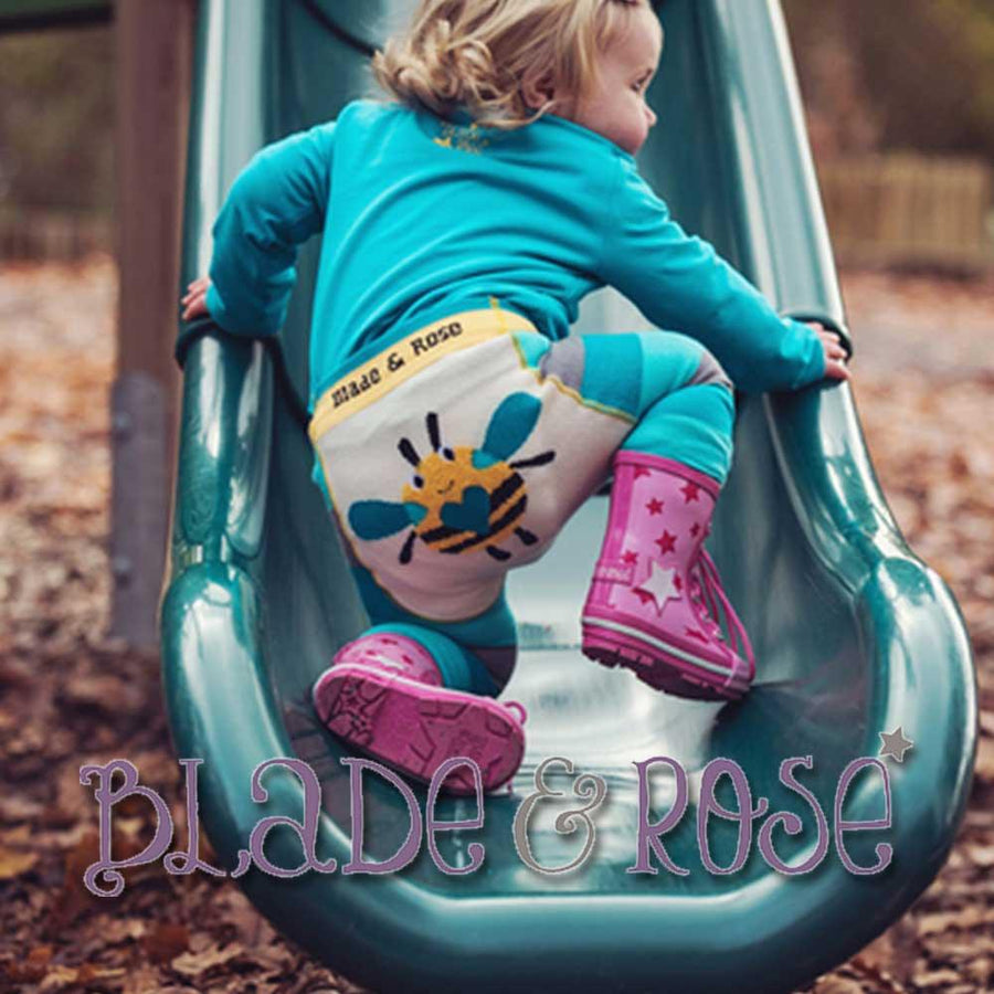 En flicka sitter i rutschkana på en lekplats och har på sig ett rosa par gummistövlar från Blade & Rose.