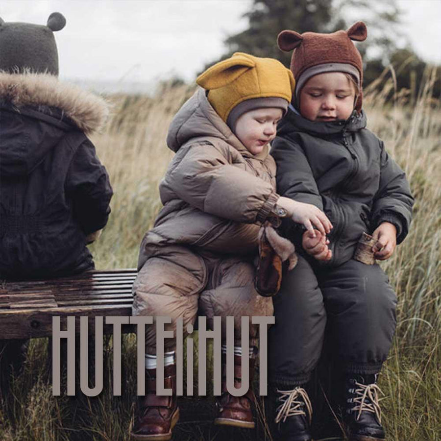 Två små barn sitter i blåsigt höstväder på en bänk och är klädda i varumärket Huttelihut.