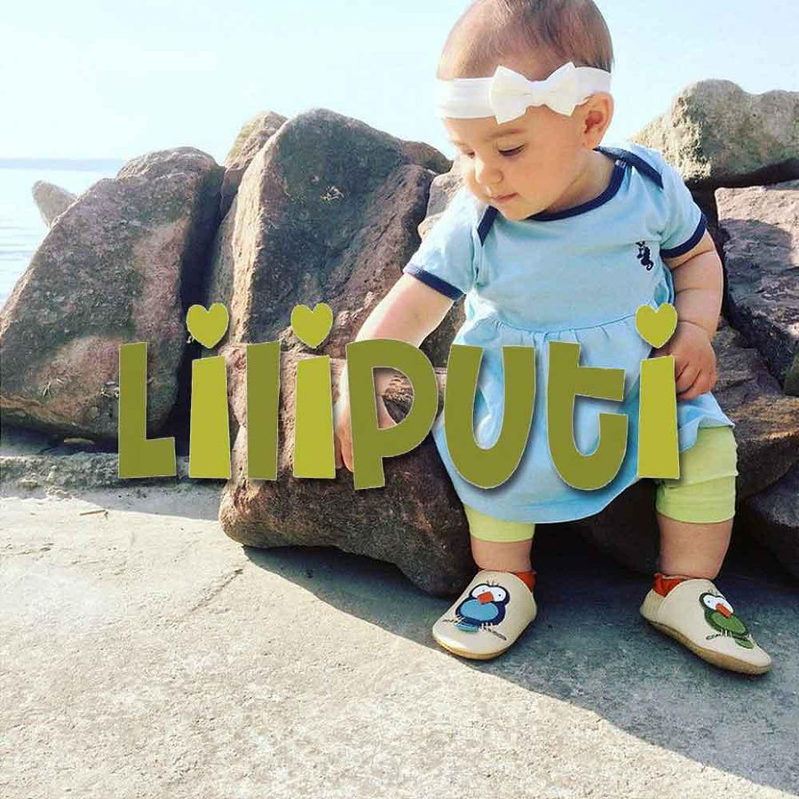 Ett litet barn står på stranden i ett par barfotatofflor från Liliputi och försöker lära sig att gå stadigt.