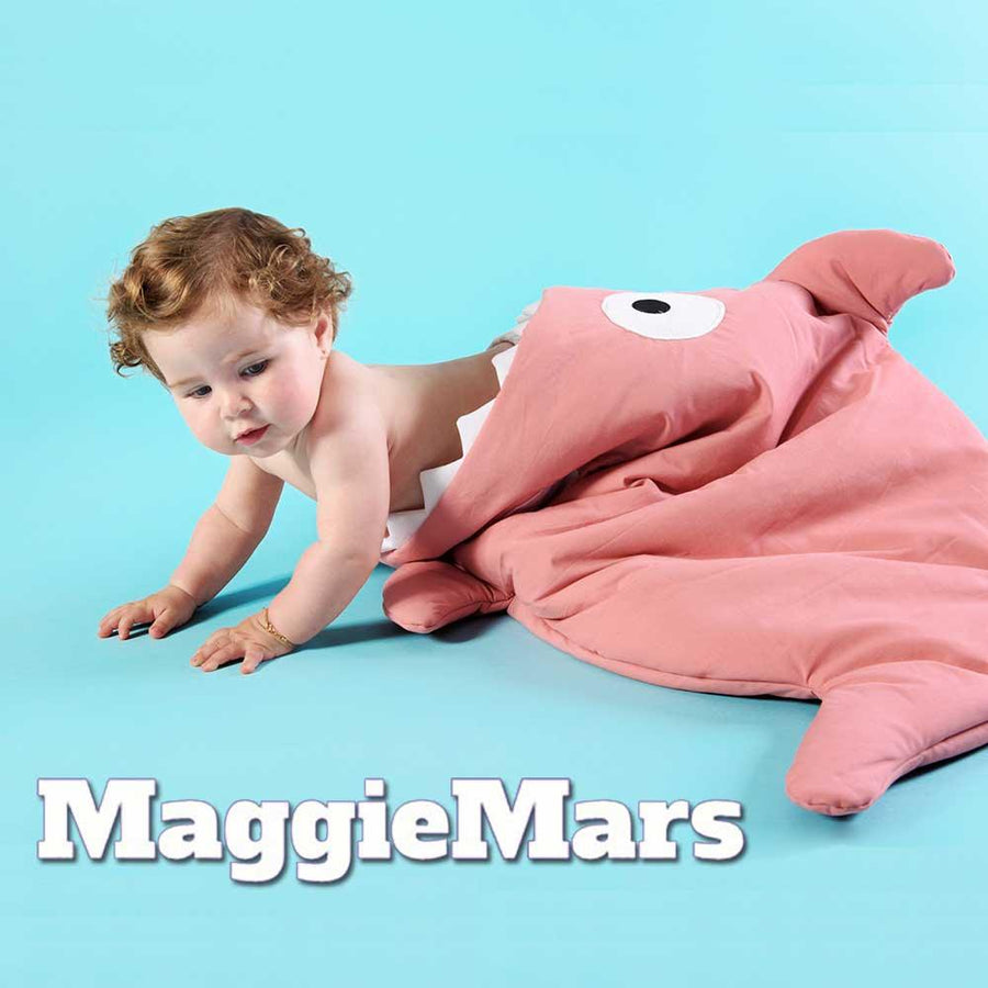 Ett ungt barn, en bebis, tittar ut från en sovpåse från varumärket MaggieMars Baby Bites som är formad som en haj.