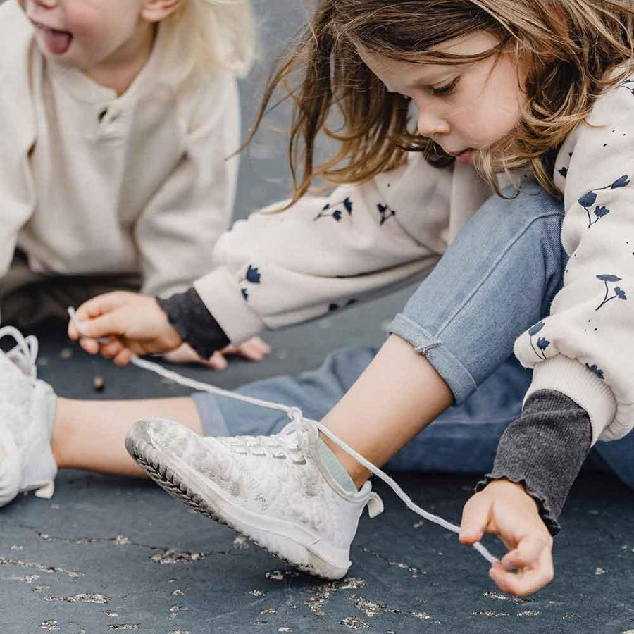 Ett barn sitter på marken och försöker knyta sina barnskor med skosnören.