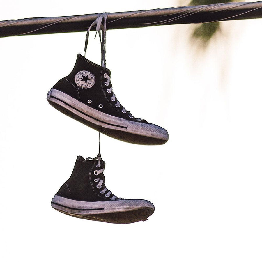 Ett par sneakers av märket Converse i modellen Chuck Taylors, hänger i sina skosnören över en stång högt upp i luften.