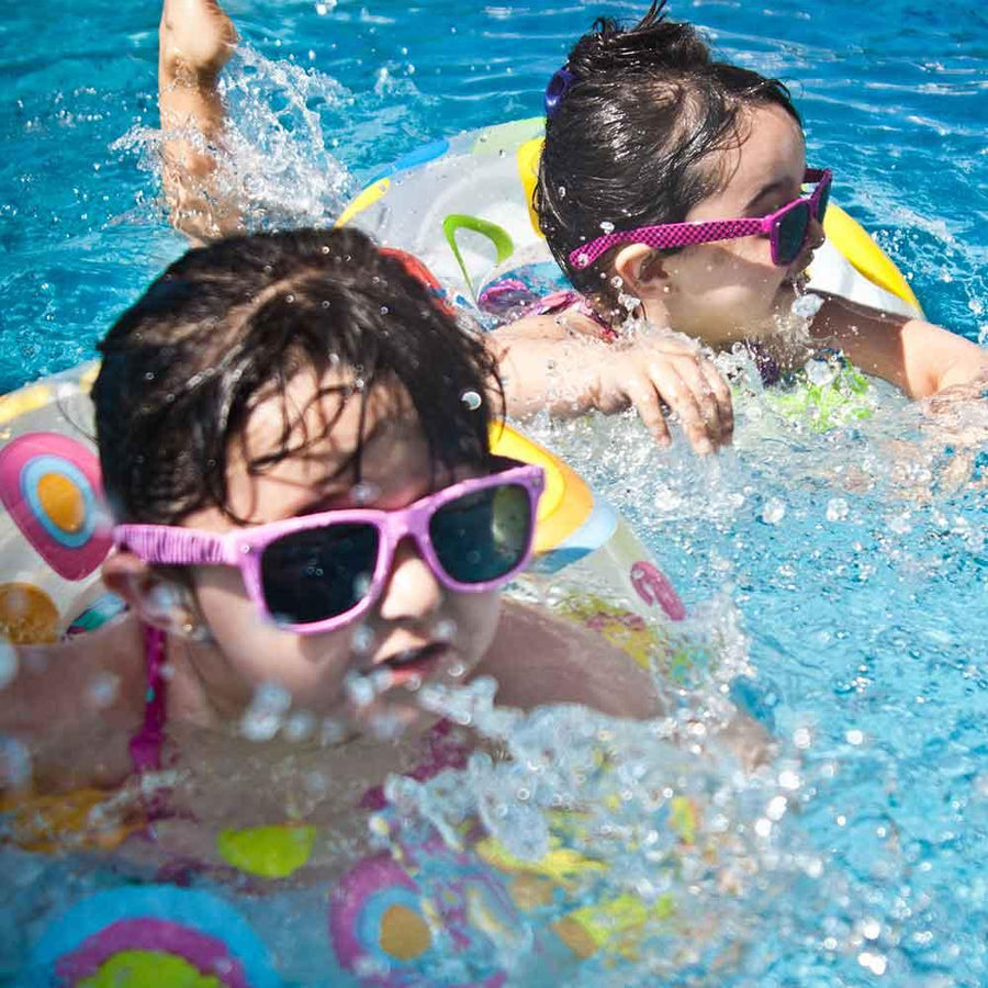 Två flickor badar under sommaren med flytleksaker i en pool med fina solglasögon som är gjorda för barn.