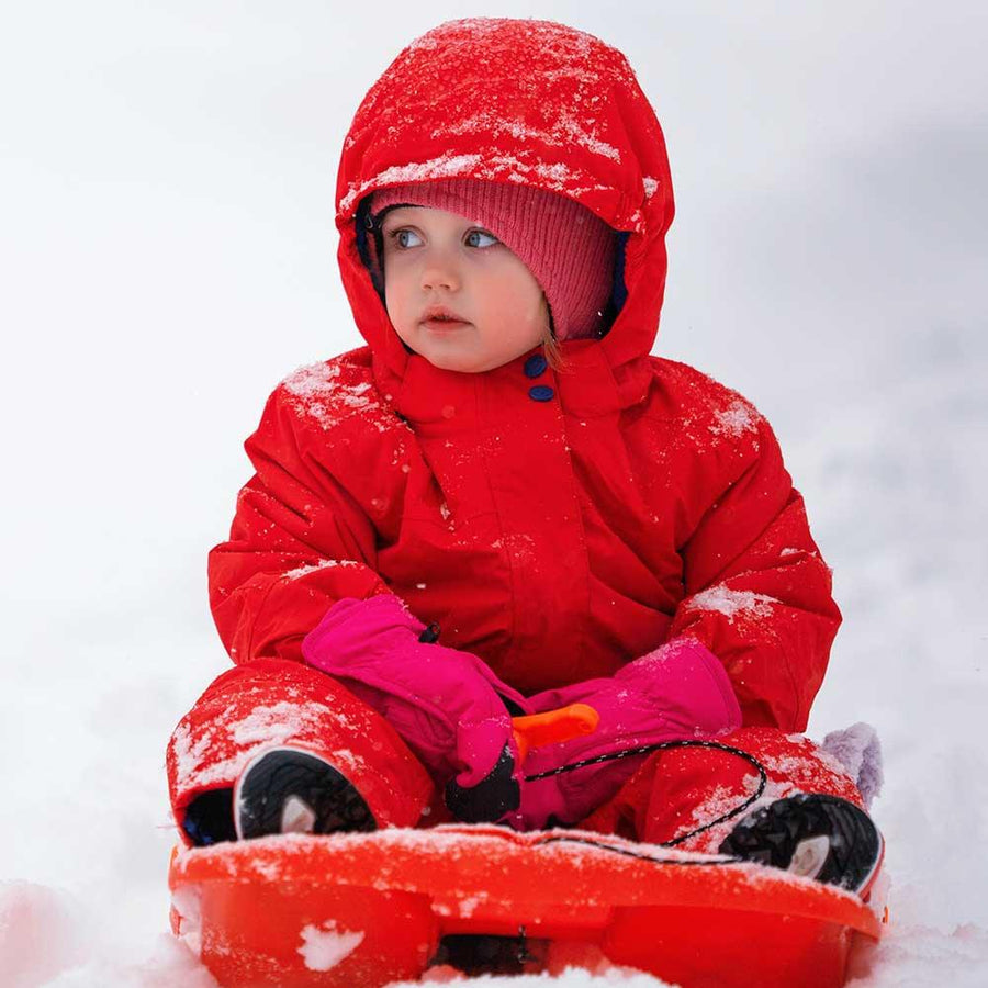 Ett barn sitter på en pulka med varma vantar på händerna under en snöfylld vinterdag.