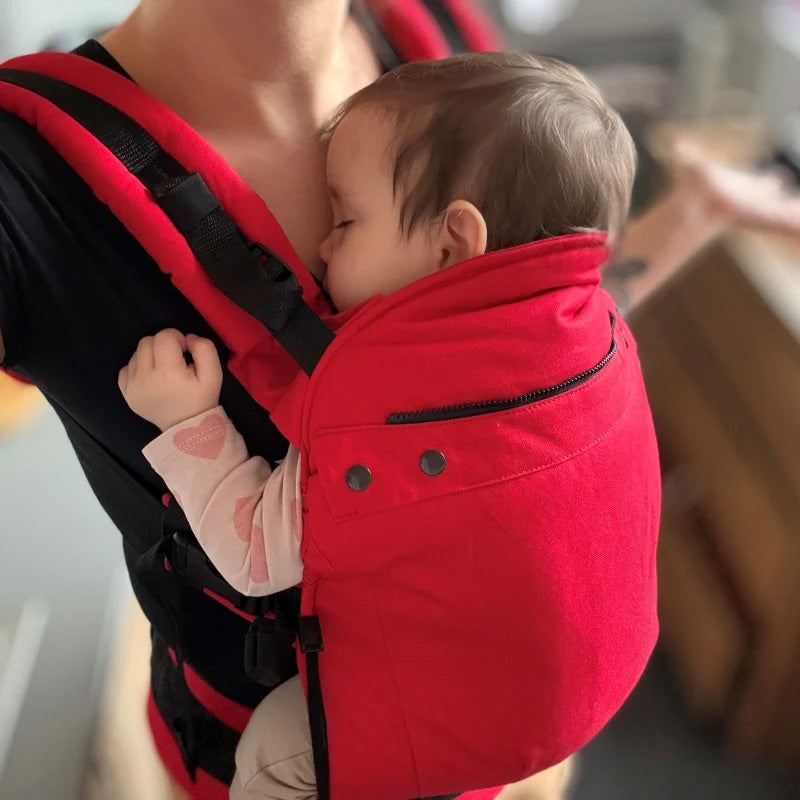 En bebis sover i en röd baby carrier från varumärket Liliputi i sin mammas famn.